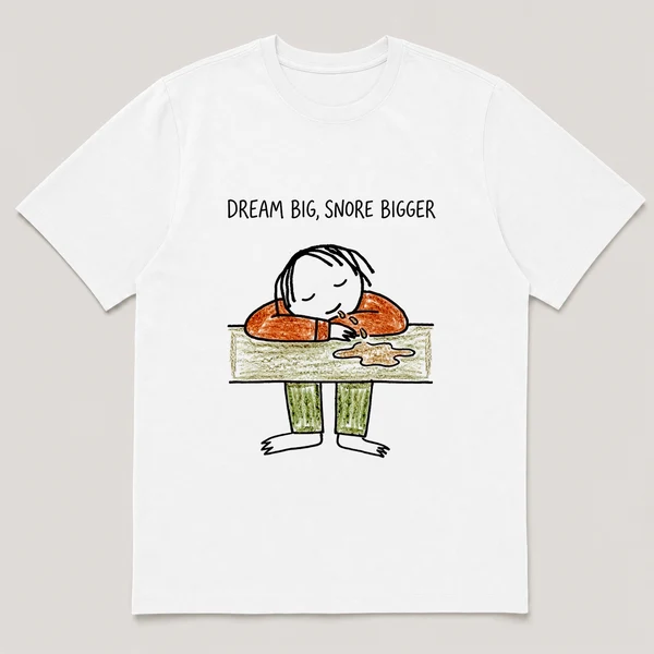 Front view of a White Tee printed with guy sleeps at a desk with his cheek on folded arms and a drool puddle and the caption DREAM BIG, SNORE BIGGER