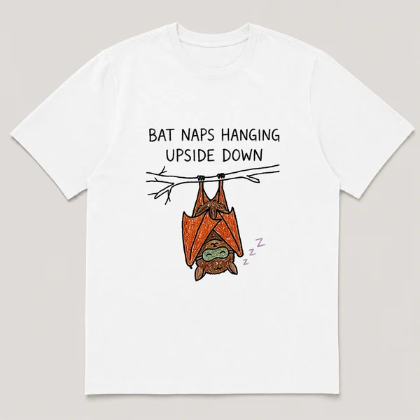 Front view of a White Tee printed with bat sleeps hanging from a branch wearing a tiny sleep mask and the caption BAT NAPS HANGING UPSIDE DOWN