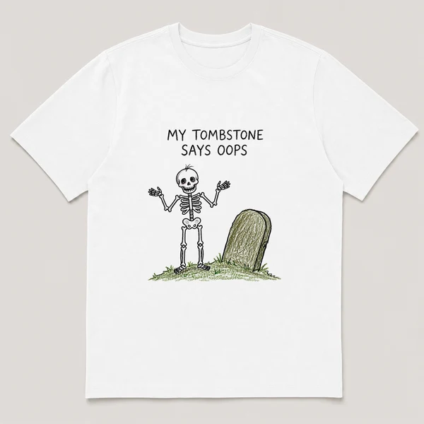 Front view of a White Tee printed with skeleton shrugs beside a lopsided tombstone on a small grassy mound and the caption MY TOMBSTONE SAYS OOPS