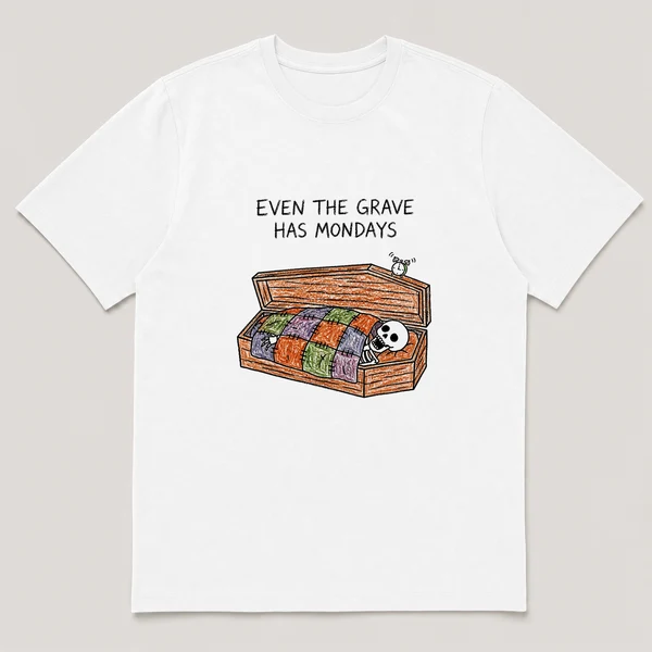 Front view of a White Tee printed with a skeleton yawns under a patchwork quilt inside an open coffin while a tiny alarm clock rings on the lid and the caption EVEN THE GRAVE HAS MONDAYS